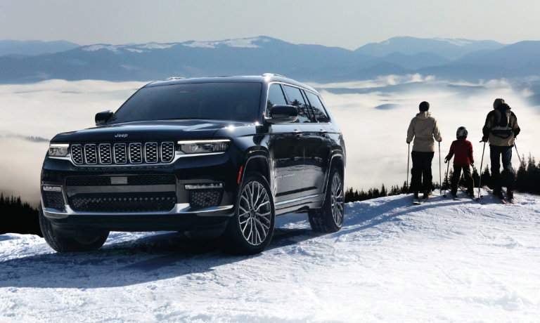 2023 Jeep Grand Cherokee L parked at top of snowy hill with skiers